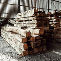 Ancient reclaimed French oak beams stacked in a warehouse, showcasing their weathered textures and unique character.