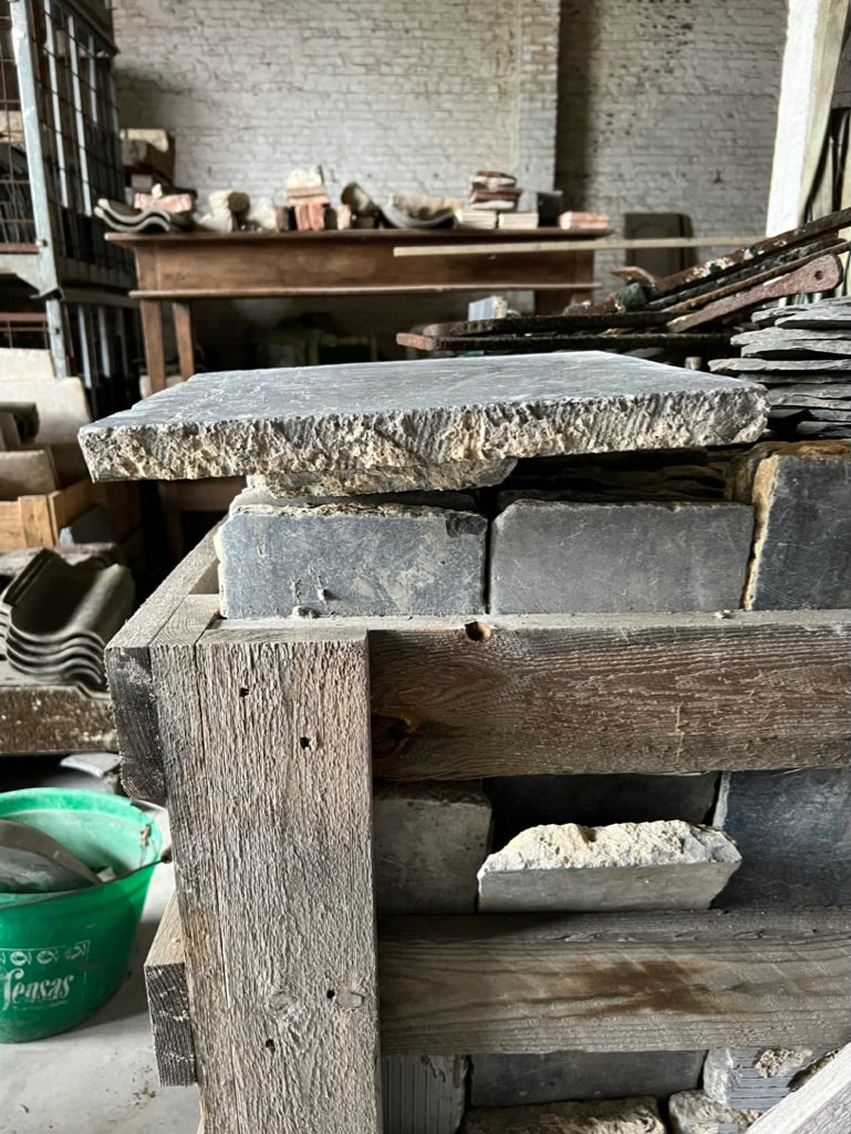 Reclaimed Belgian Bluestone Tiles with weathered texture and rich patina stacked in a rustic indoor setting