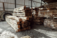 Ancient reclaimed French oak beams stacked in a warehouse, showcasing their weathered textures and unique character.