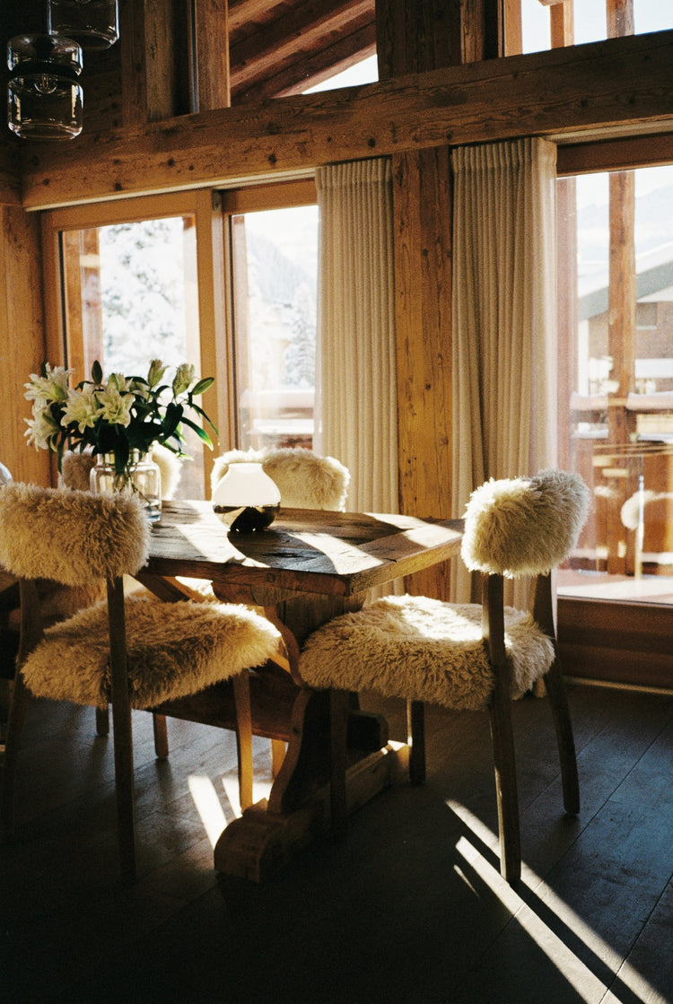 Swiss chalet dining corner with old timber walls and sheepskin chairs